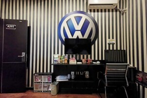 Una habitación con pared a rayas, un refrigerador A203 negro, un escritorio con varios objetos y un logotipo de VW en la pared.