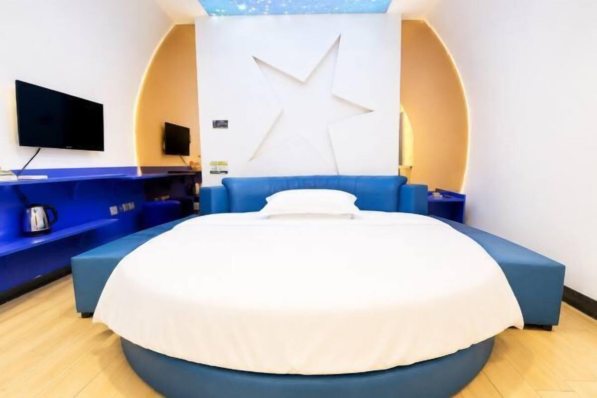 Une chambre d’hôtel moderne dotée d’un grand lit, d’un téléviseur à écran plat, d’une décoration murale en forme d’étoile et d’un coin salon bleu.