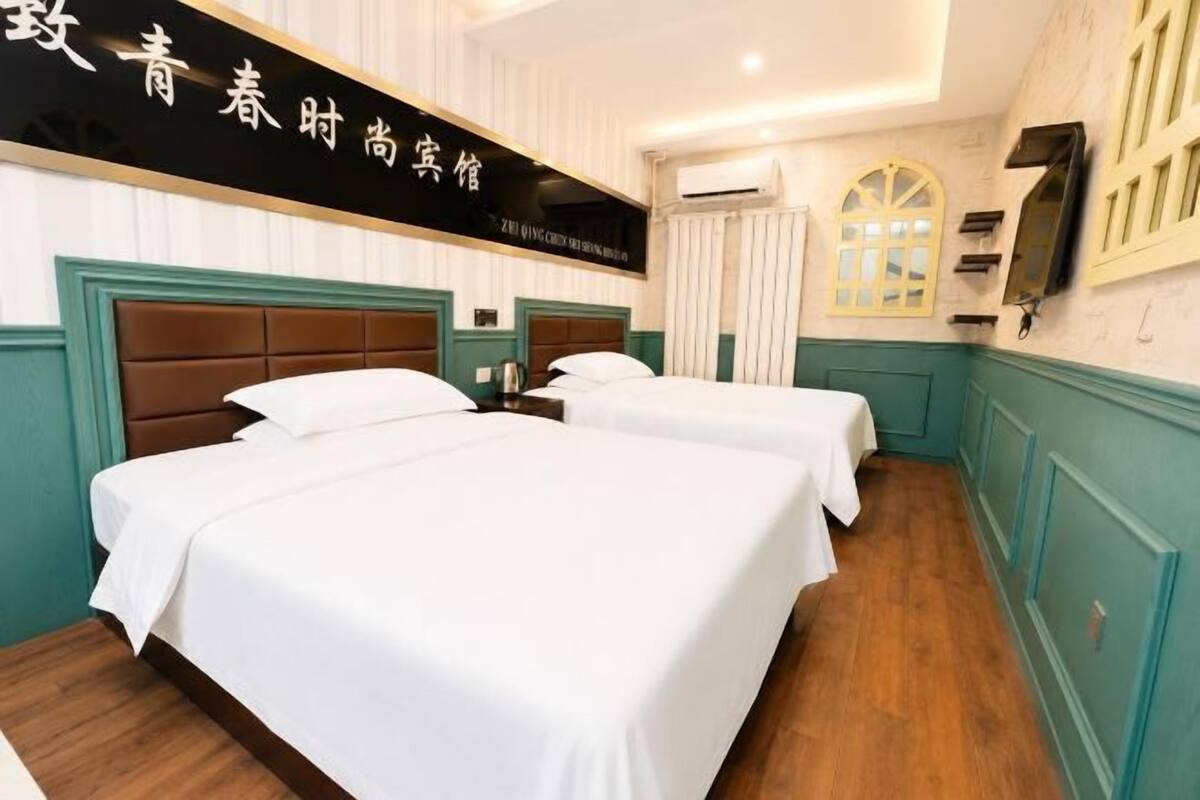 Une chambre d’hôtel avec deux lits, un plancher en bois, un plafond blanc et un téléviseur fixé au mur.