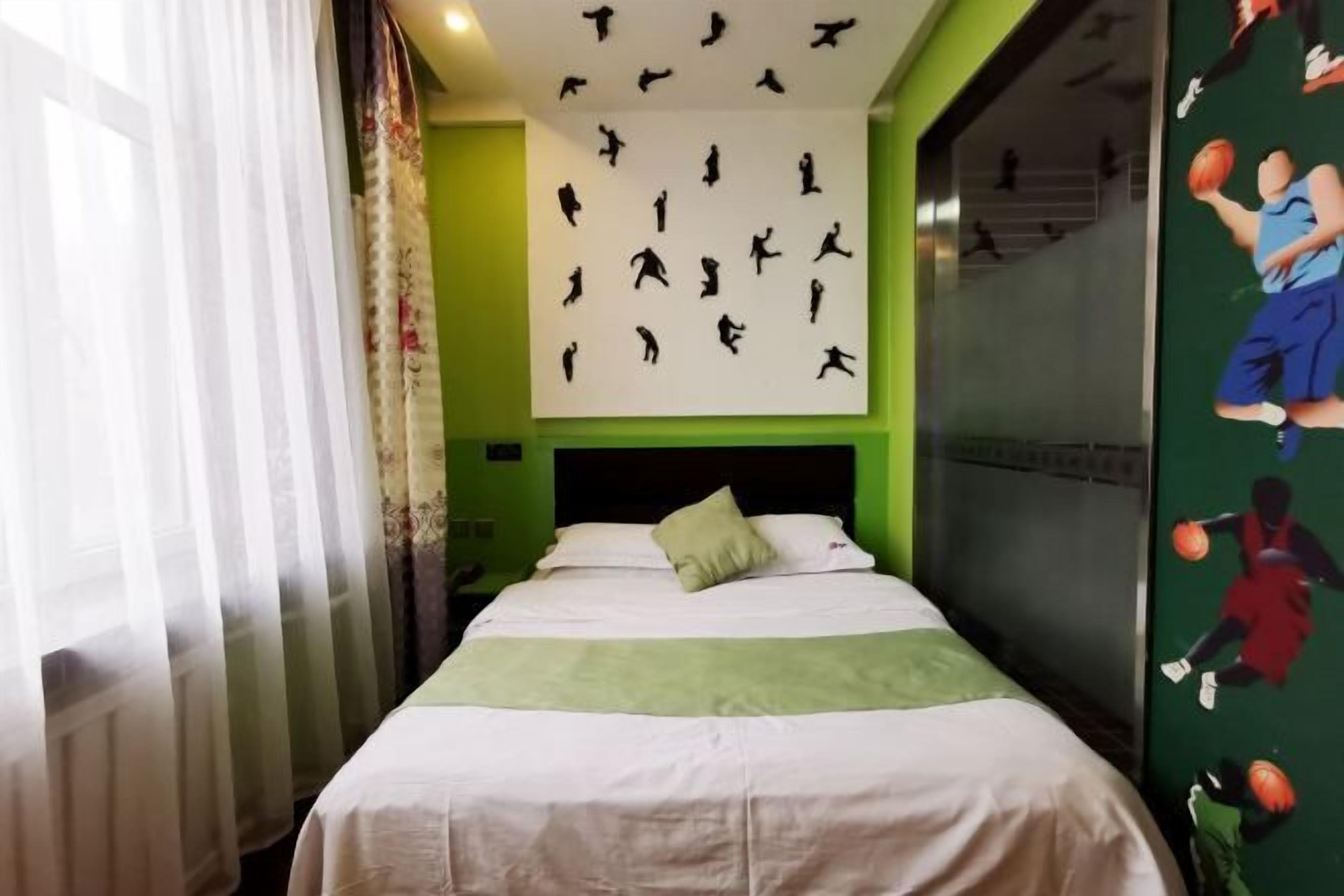 Ein Hotelzimmer mit Bett, grünen Wänden, einem Wandgemälde zum Thema Basketball und einem Fenster mit transparenten Vorhängen.