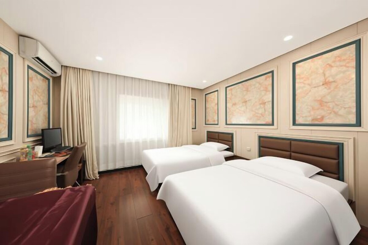 A hotel room with two beds, a desk, a TV, and artwork on the walls.