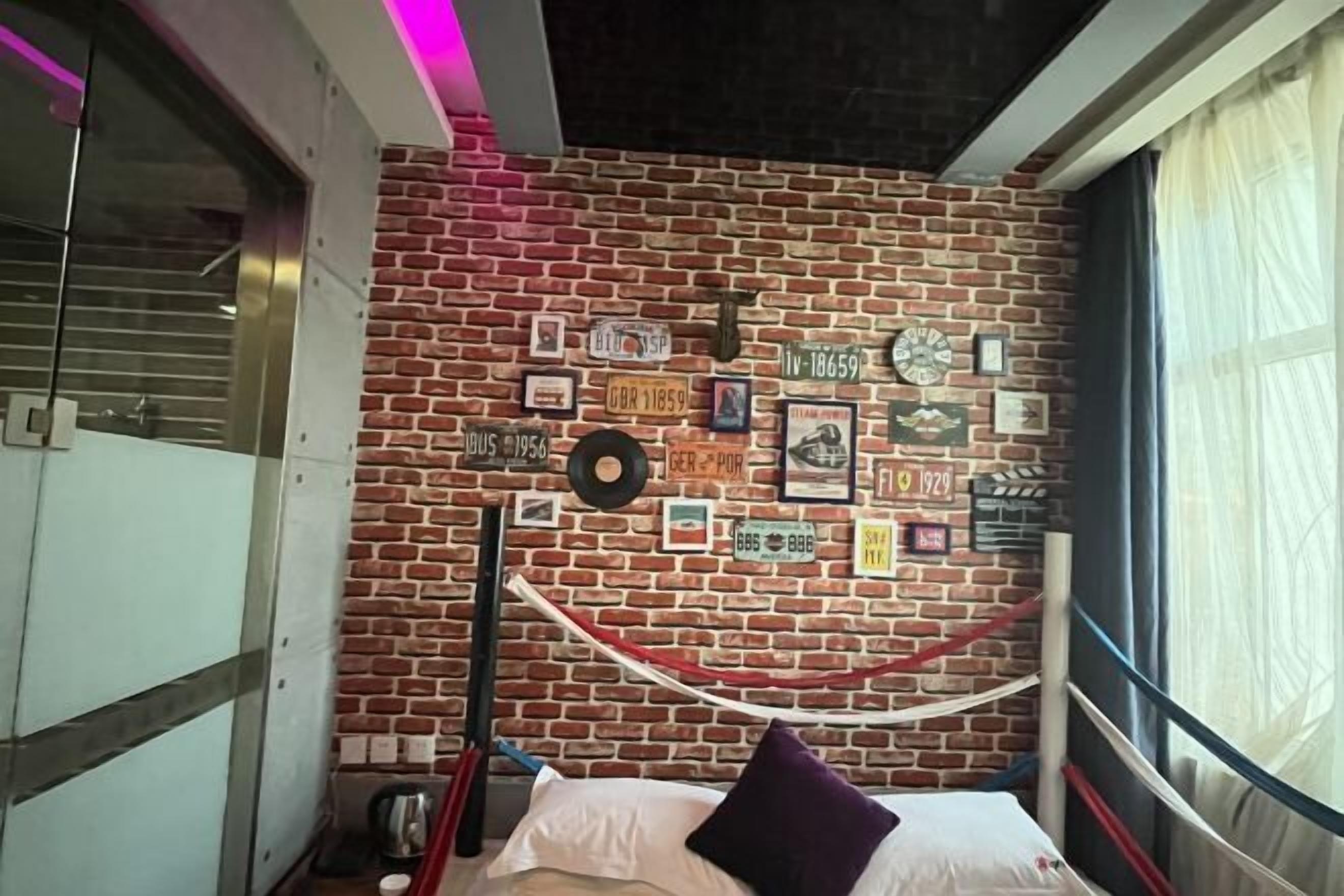 A room with a brick wall, a bed with a pillow, a window with curtains, and a red and white rope decoration.