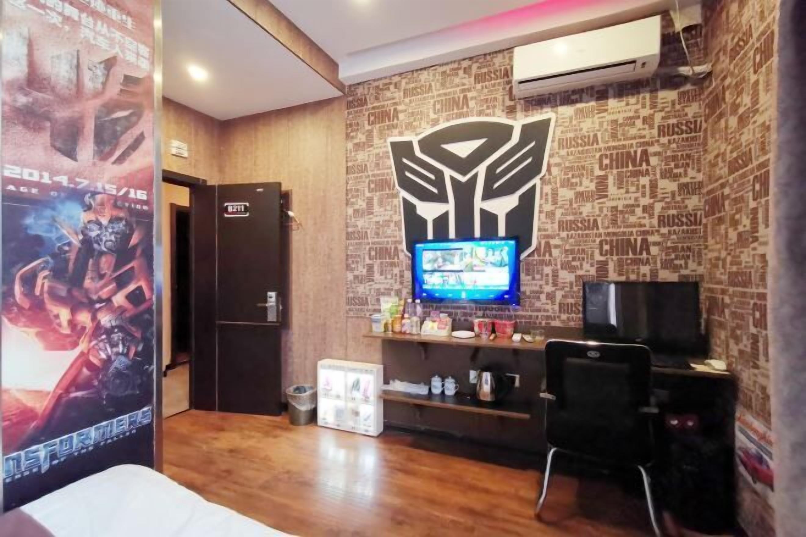 Habitación de hotel con piso de madera, televisor en la pared, escritorio con computadora y un cartel de un videojuego.