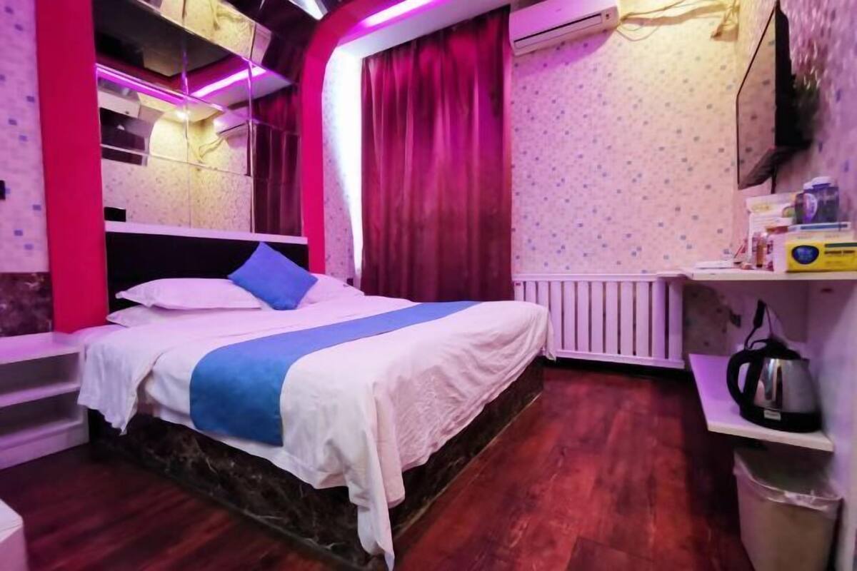 Une chambre à coucher avec un lit, un radiateur, une étagère avec des objets et une fenêtre avec des rideaux.