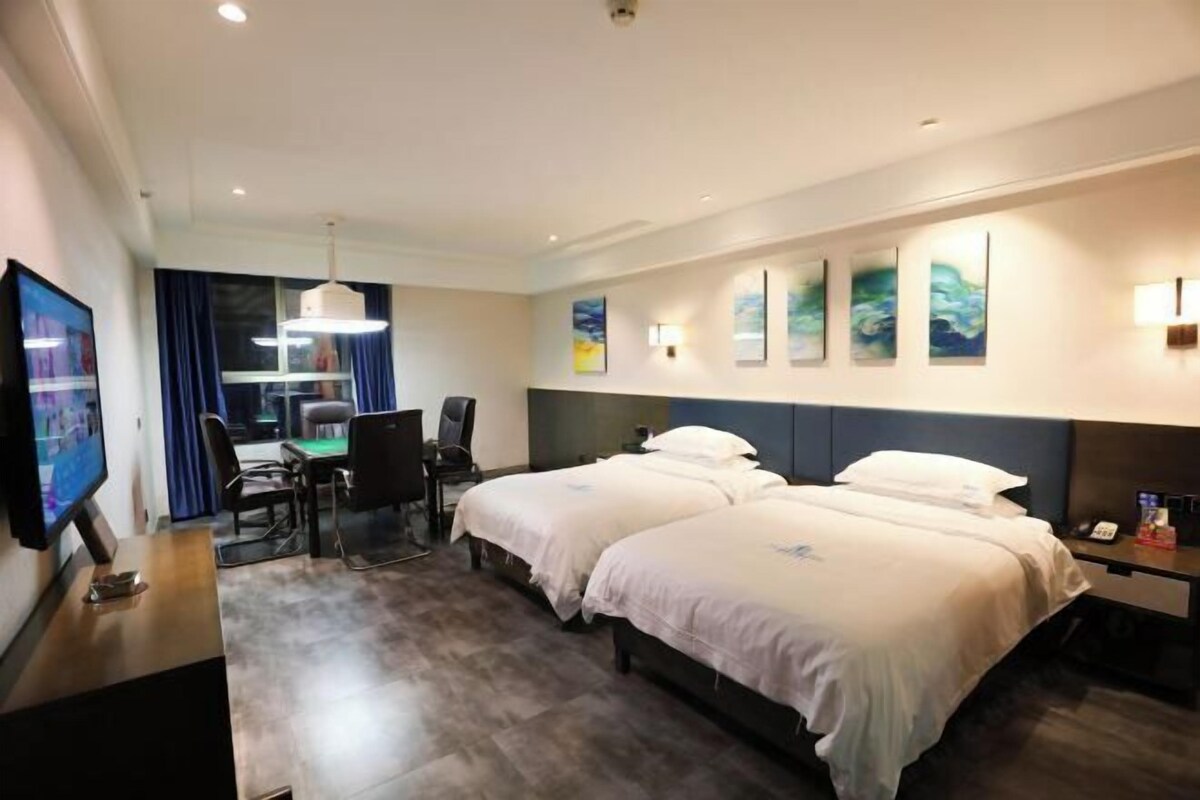 Une chambre d’hôtel avec deux lits, un bureau avec un ordinateur, une télévision et des œuvres d’art accrochées aux murs.