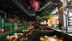 Een restaurant met houten tafels en groene banken, versierd met hangplanten en een neonreclame.