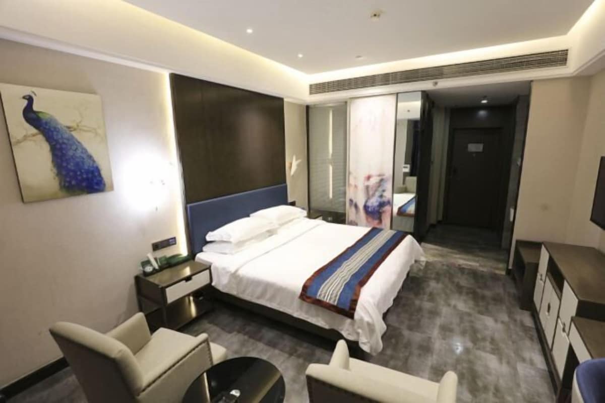 Une chambre d’hôtel avec un lit, des tables de chevet, un bureau, une chaise, une télévision et un tableau représentant un paon accroché au mur.