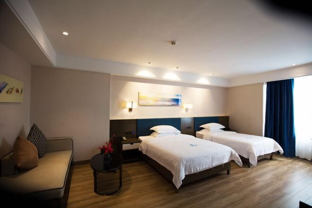 Une chambre d’hôtel avec deux lits, un canapé, une petite table ornée de fleurs et un tableau au mur.