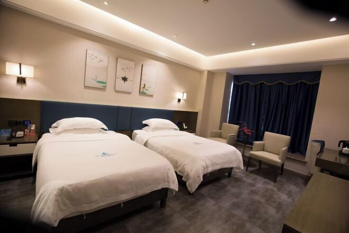 Une chambre d’hôtel avec deux lits, un bureau, une chaise et des œuvres d’art accrochées aux murs.