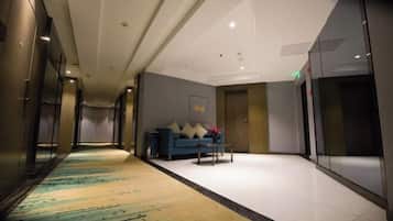 Un pasillo de hotel con alfombra estampada, un sofá azul con cojines y una pequeña mesa.