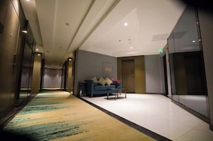 Un pasillo de hotel con alfombra estampada, un sofá azul con cojines y una pequeña mesa.