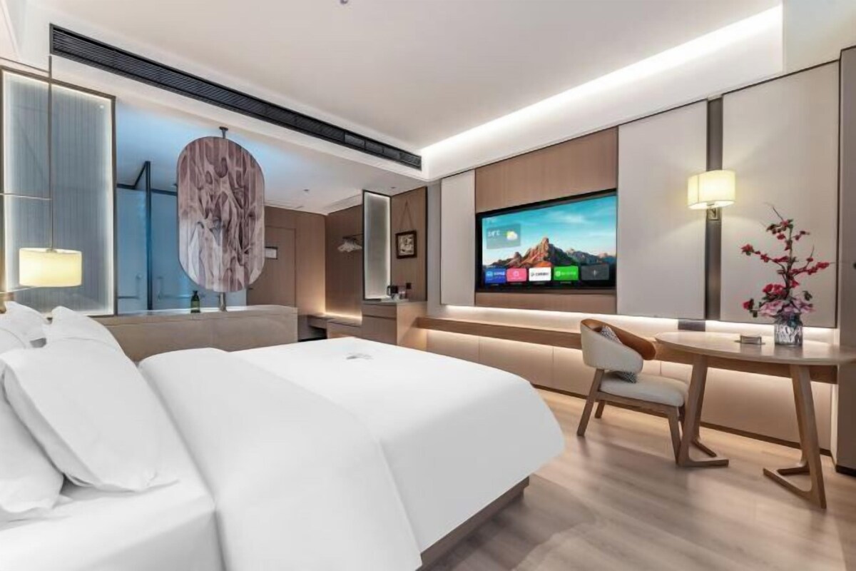 Une chambre d’hôtel moderne équipée d’un lit, d’un bureau, d’une télévision et d’un grand miroir.