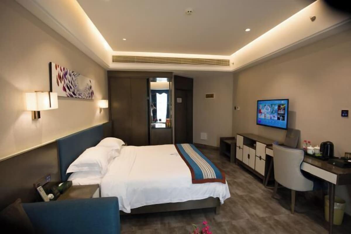 Une chambre d’hôtel moderne, équipée d’un lit, d’une table de chevet, d’un bureau, d’une chaise, d’une télévision et d’œuvres d’art accrochées aux murs.