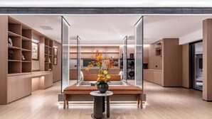 Een moderne hotellobby met een centraal zitgedeelte, een bloevas en een grote spiegel die de ruimte weerspiegelt.