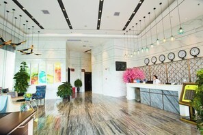 Un hall d’hôtel avec un sol en marbre, un comptoir d’accueil, plusieurs horloges et des plantes en pot.