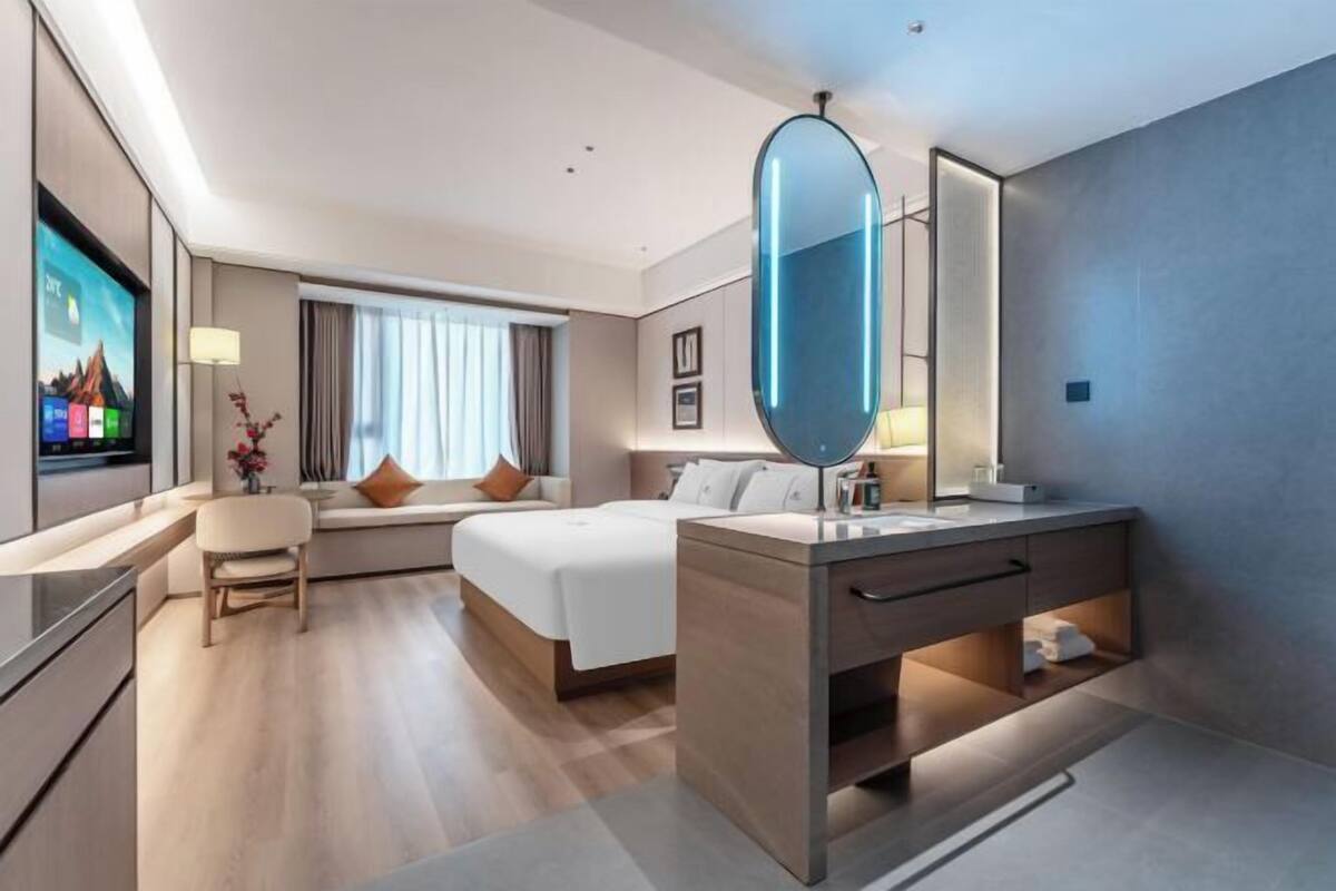 Een moderne hotelkamer met een bed, een bureau, een televisie, een grote spiegel en een badkamer met een wastafel en spiegel.