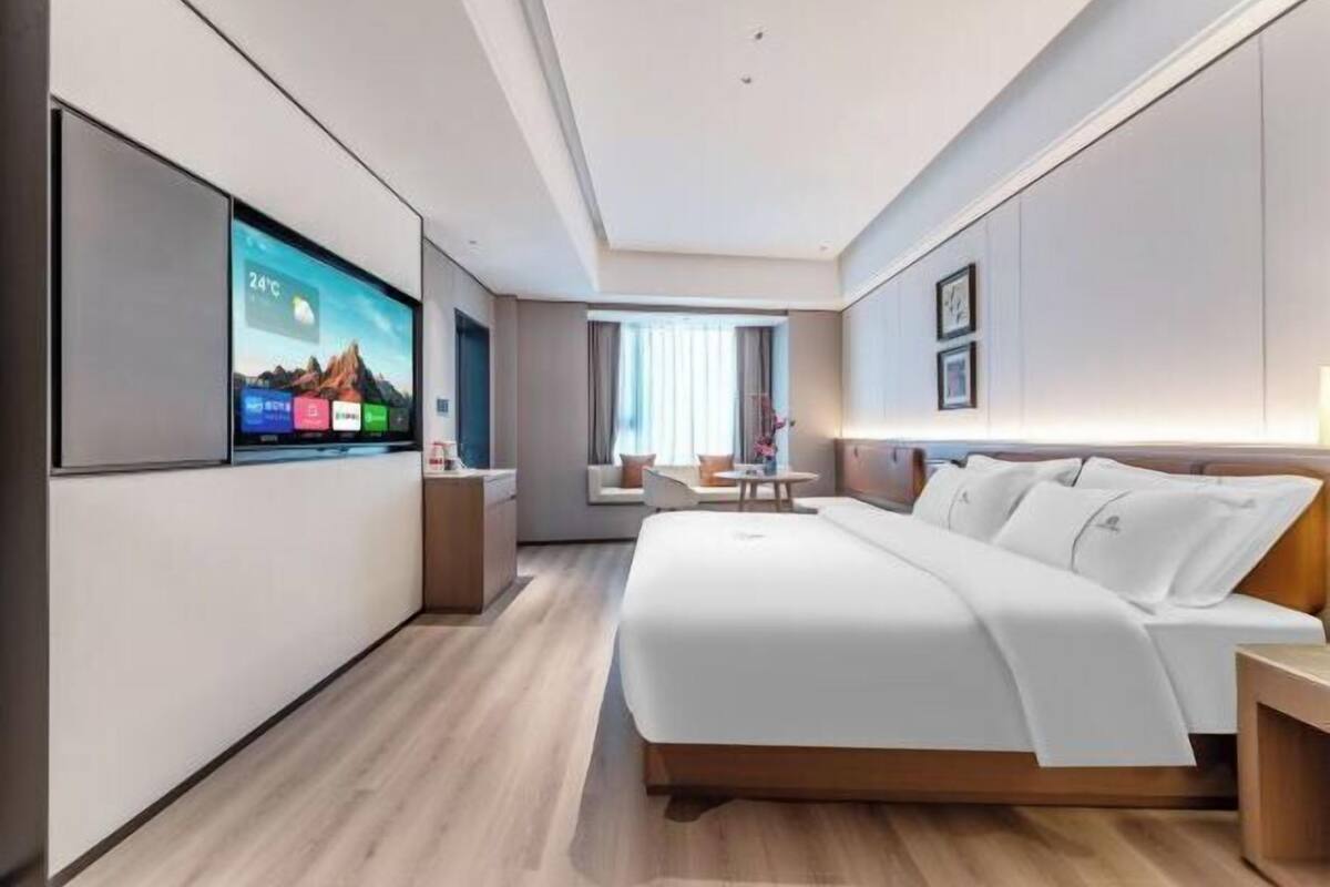 Een moderne hotelkamer met een groot bed, een tv aan de muur, een zithoek met een tafel en een raam met gordijnen.