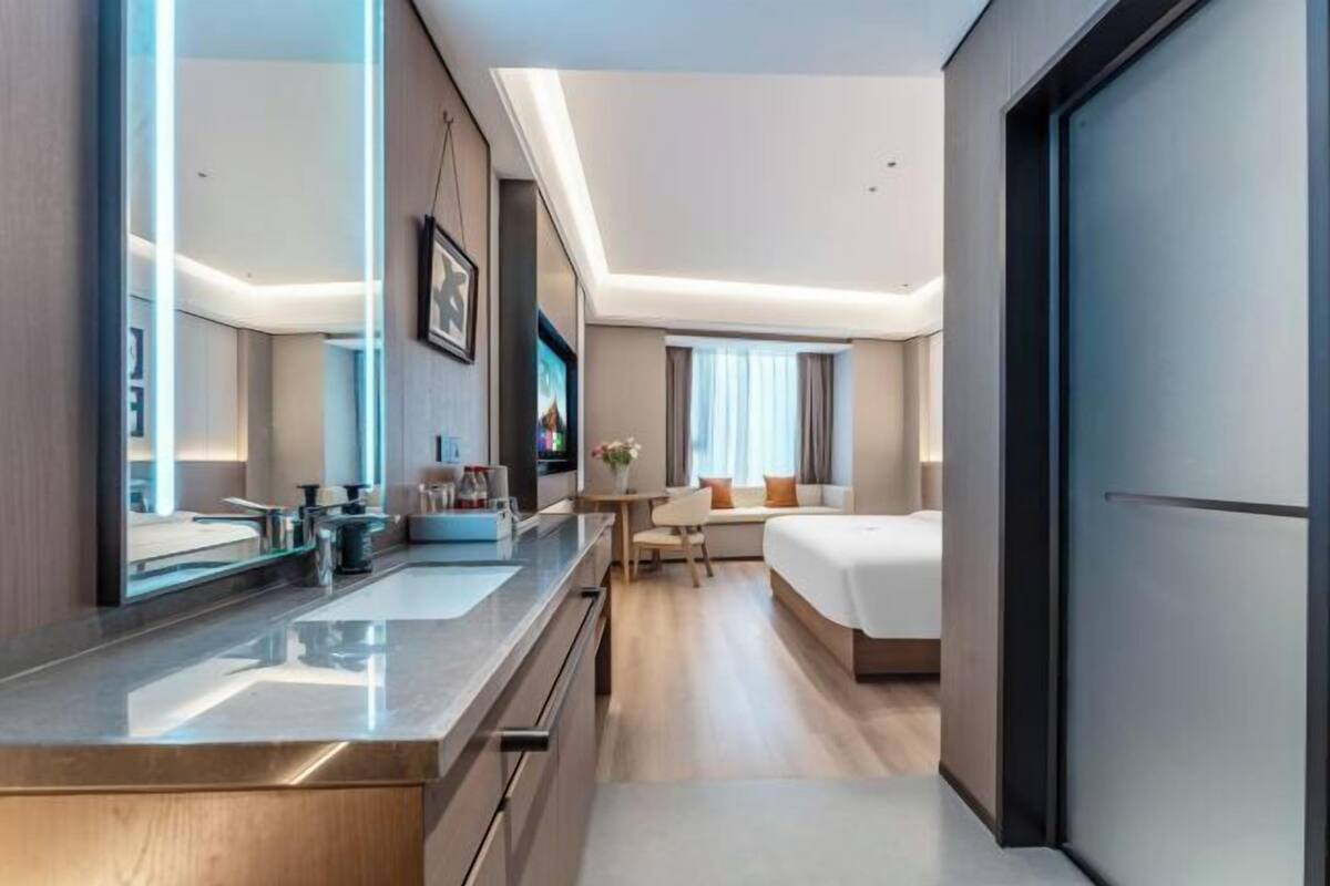 Een moderne hotelkamer met een groot bed, een aparte zithoek, een kitchenette en een grote spiegel.