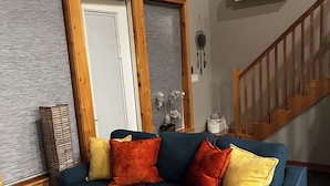Un salón con un sofá modular, una escalera de madera y un equipo de aire acondicionado.