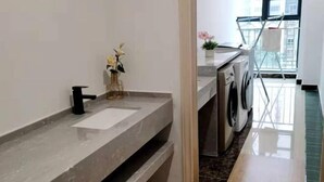 A modern bathroom with a marble sink, a black faucet, and a vase with flowers. There is a washing machine and a drying rack in the background.