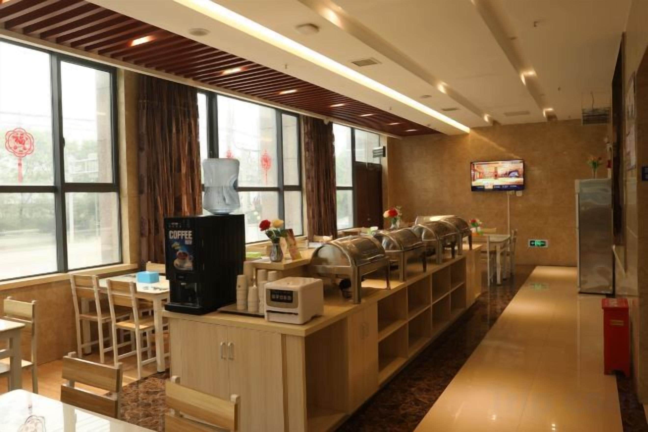 Area colazione in hotel con macchina del caffè, buffet, posti a sedere e schermo televisivo.