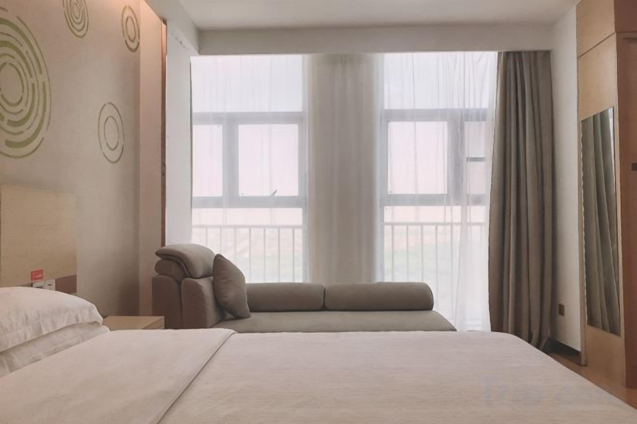A hotel room with a large bed, a seating area, a nightstand, and a window with curtains.