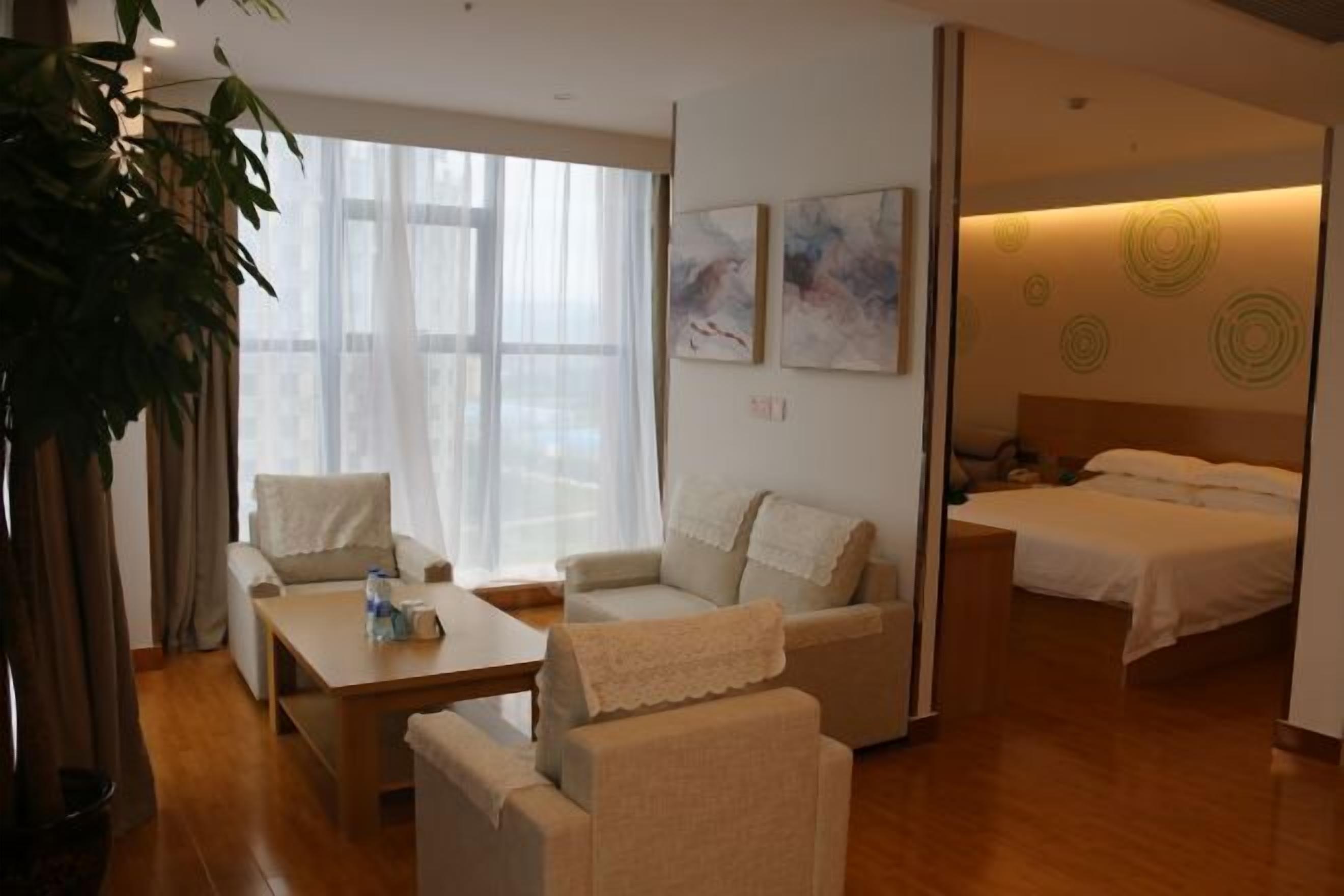 Une chambre d’hôtel avec un lit, deux canapés, une table basse et une grande fenêtre avec des rideaux.