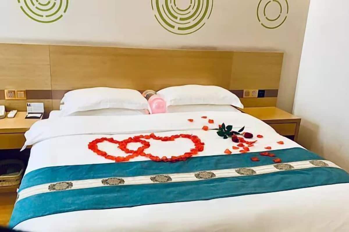 Habitación de hotel con cama, cabecera de madera, mesita de noche y teléfono, y pared con diseños circulares.