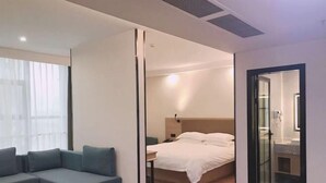 A modern hotel room with a sofa, a bed, a desk, and a bathroom visible through a glass door.
