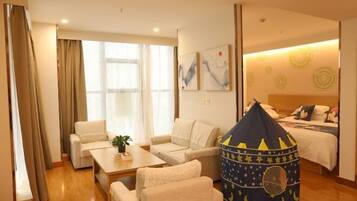 A hotel room with a bed, a sofa, a small table, a window with curtains, and a tent-like play area.