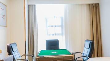 A hotel room with a pool table, two chairs, a bed, and a window with curtains.