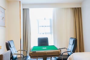 A hotel room with a pool table, two chairs, a bed, and a window with curtains.