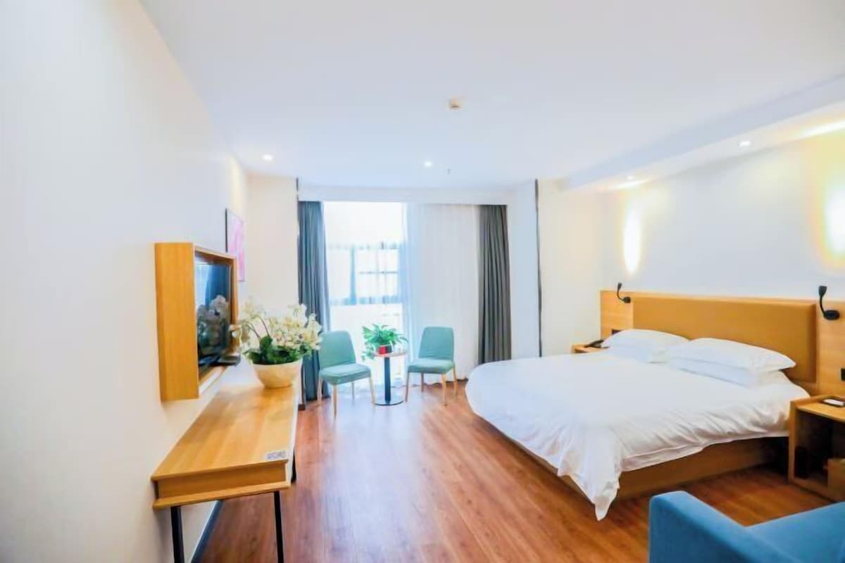 Quarto de hotel com cama, mesa de cabeceira, cadeira, mesinha com uma planta e vista para o exterior.