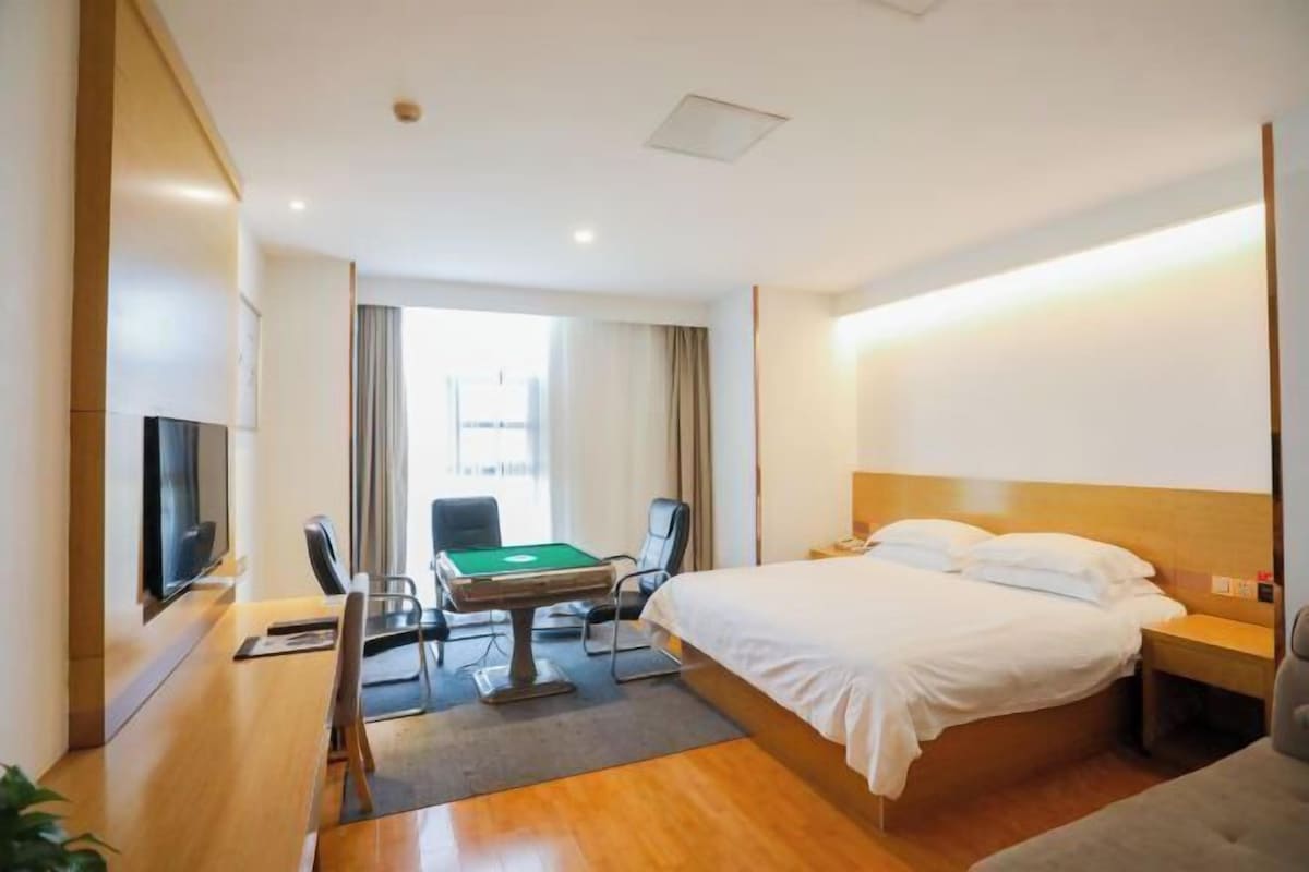 Quarto de hotel com cama, escrivaninha com mesa de bilhar, televisão e janela com cortinas.