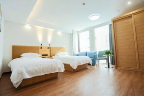 Quarto de hotel moderno com duas camas, cabeceira de madeira, uma mesinha e vista para o exterior.