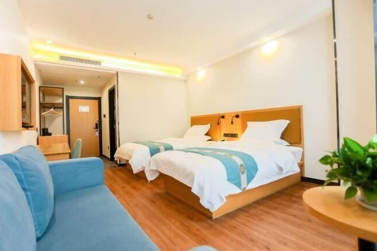 Habitación de hotel con dos camas, un sofá azul, una mesita y una planta.