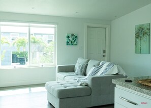 Relax in this stylish living room with a sofa, ottoman, and artwork, offering a view of the outside.