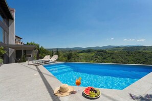 Une piscine avec vue sur les montagnes, un fauteuil de relaxation et un assortiment de fruits frais.