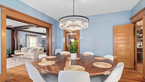 A dining room with a round wooden table, white chairs, and a chandelier.
