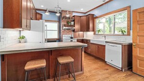 A kitchen with wooden cabinets, a large island with stools, a brick backsplash, and a dishwasher.
