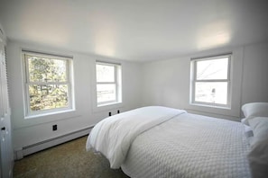 Un dormitorio con una cama grande, tres ventanas y un radiador.