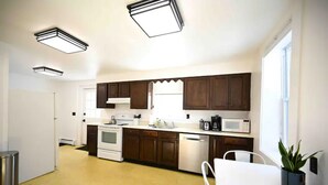 Una cocina moderna con armarios de madera oscura, encimeras blancas, un lavamanos de acero inoxidable y una estufa blanca. Hay una ventana que proporciona luz natural y una planta en maceta sobre la encimera.