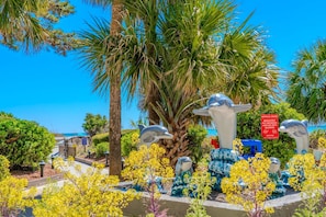 Un jardín con esculturas de delfines, palmeras y flores amarillas.