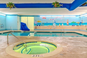An indoor swimming pool with a mural of a beach scene, a shallow water sign, and a no diving sign.