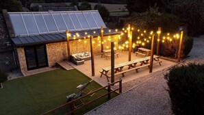 Ein Patio mit Lichterketten, Holzbanken und einem Steinhaus mit Glastür.