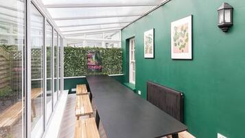 A conservatory with a long table and benches, green walls, and framed botanical prints.