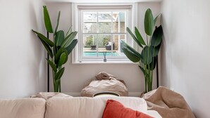 Ein Eckzimmer mit weißer Wand, einem Fenster mit Blick auf einen Pool und zwei großen, grünen Pflanzen.