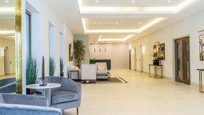 Een ruime, moderne lobby met een grijze bank, een ronde tafel en een potplant.
