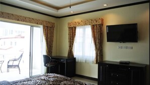 A hotel room with a bed, a desk, a chair, a TV, and a balcony with a chair. - Baan Suan Lalana Sa Floor 5 Room 518 (Pattaya)