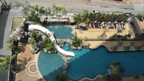 A rooftop pool area with a waterfall feature, sun loungers, and palm trees. - The Cliff Condominium Floor 10th Number 1007 (Pattaya)